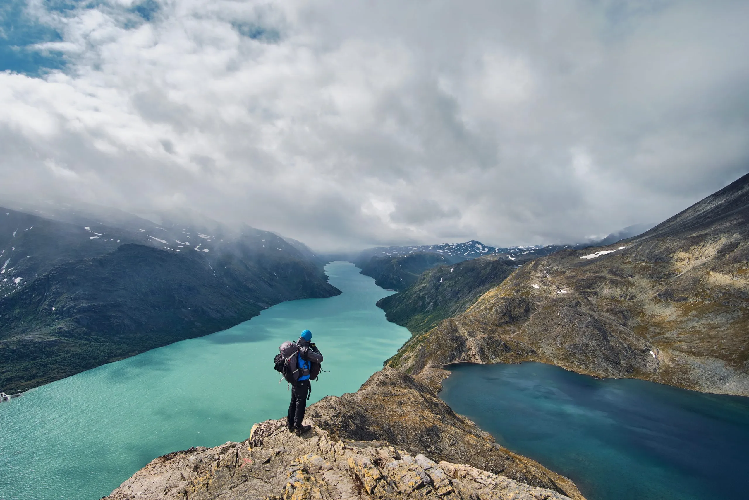 Junger Wanderer mit Rucksack genießt die Aussicht auf den Besseggen-Grat und den Gjende-See im Jotunheimen-Nationalpark in den norawischen Bergen